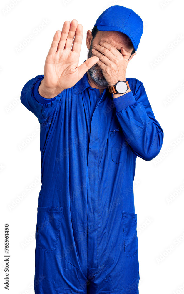 Middle age handsome man wearing mechanic uniform covering eyes with hands and doing stop gesture with sad and fear expression. embarrassed and negative concept.