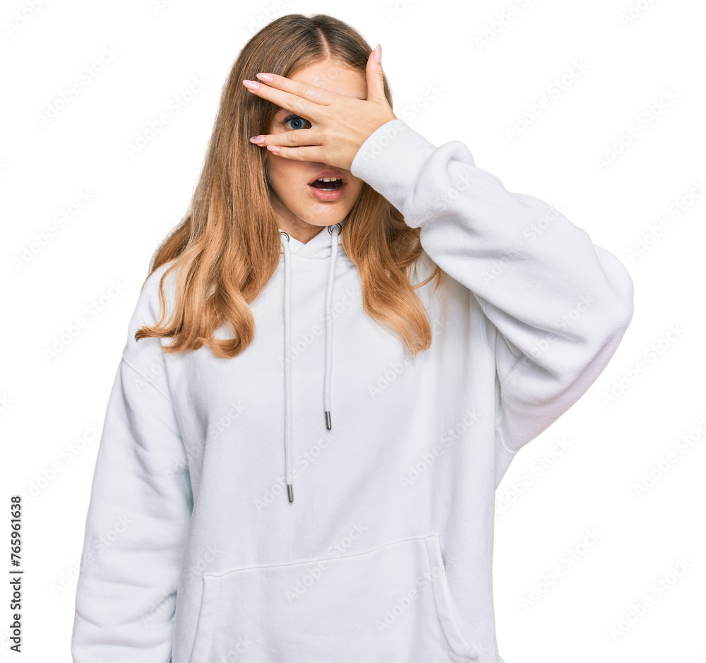 Beautiful young caucasian girl wearing casual sweatshirt peeking in shock covering face and eyes with hand, looking through fingers with embarrassed expression. Beautiful young caucasian girl wearing casual sweatshirt peeking in shock covering face and eyes with hand, looking through fingers with embarrassed expression.
