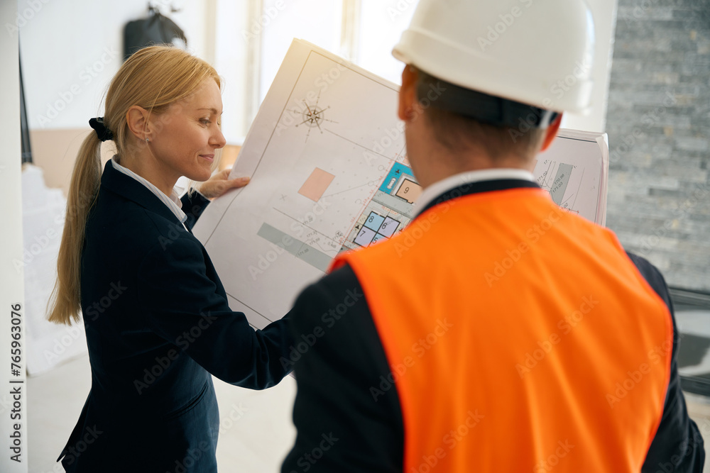 Businesswoman and engineer standing in room and looking at plan Businesswoman and engineer standing in room and looking at plan