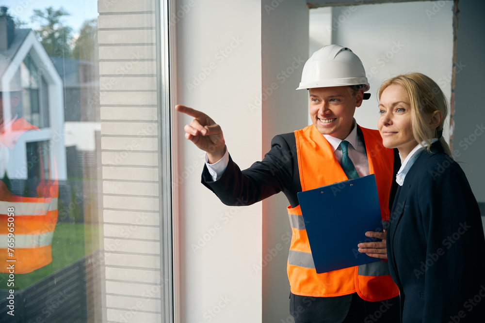 Smiling engineer and businesswoman standing and looking out window Smiling engineer and businesswoman standing and looking out window