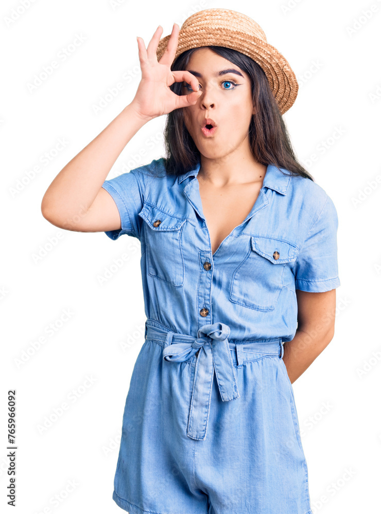 Brunette teenager girl wearing summer hat doing ok gesture shocked with surprised face, eye looking through fingers. unbelieving expression. Brunette teenager girl wearing summer hat doing ok gesture shocked with surprised face, eye looking through fingers. unbelieving expression.