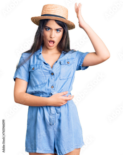Brunette teenager girl wearing summer hat surprised with hand on head for mistake, remember error. forgot, bad memory concept.