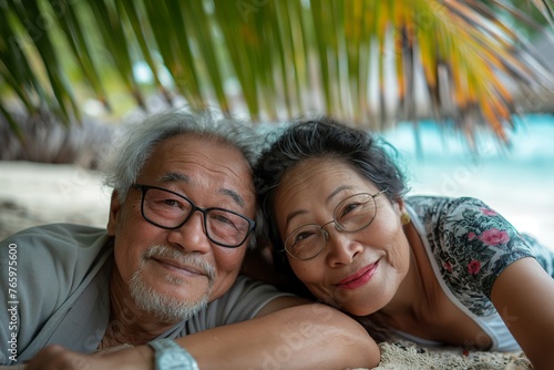 Fototapeta Naklejka Na Ścianę i Meble -  Man and woman, Asian seniors, peacefully embrace on beach under palm tree, basking in love and natures beauty.