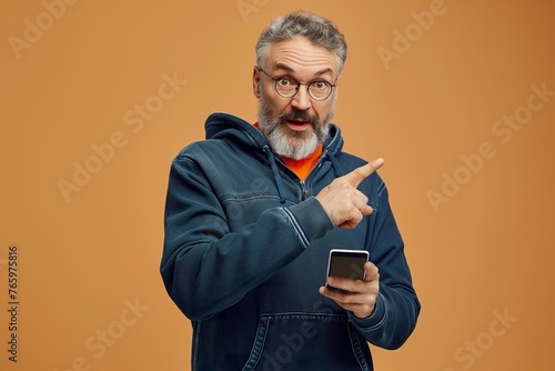 Handsome mature man with beard and glasses looking surprised while holding a cell phone. © Joaquin Corbalan