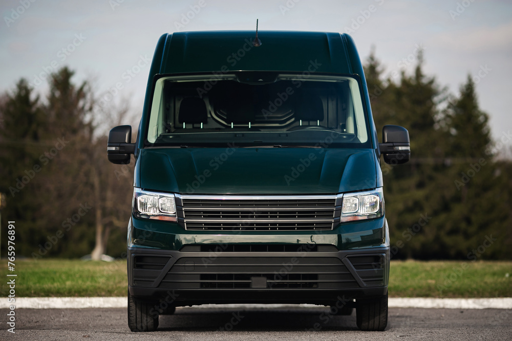 Modern van of green color on the street. The front part of the minibus, delivery car, headlights, grille.