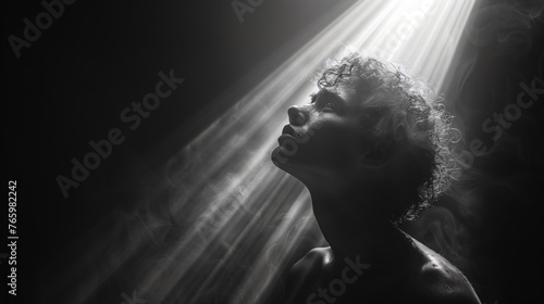silhouette of a man looking up with a light shining on him, sad in search of hope 