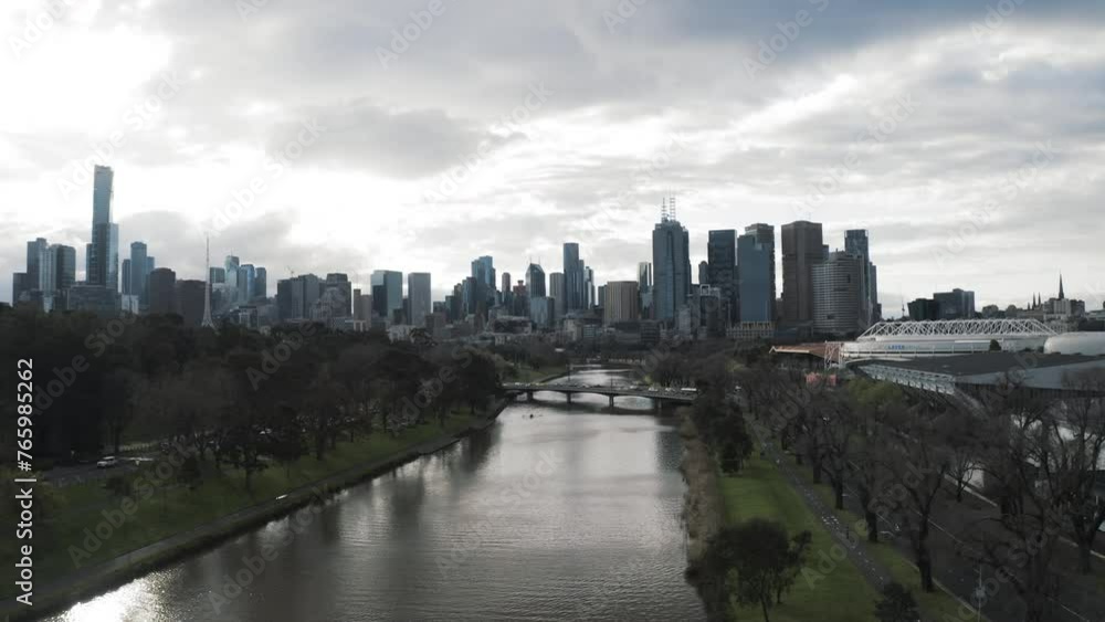 Aerial Shot Of Multipurpose Arena By Modern Buildings In City, Drone Flying Backwards Over Rippled River Under Clouds - Melbourne, Australia Aerial Shot Of Multipurpose Arena By Modern Buildings In City, Drone Flying Backwards Over Rippled River Under Clouds - Melbourne, Australia