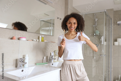 A woman by the sink in a bathroom  brushing her teeth and giving a thumbs up