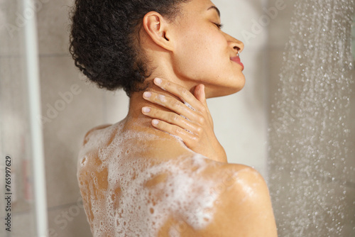 A woman lathers soap on her shoulder while taking a shower
