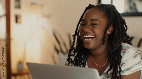 Happy black woman working remotely from home smiling on virtual meeting video call socialising with colleagues. Positive and flexible remote work culture. Candid afro american female digital on laptop photo