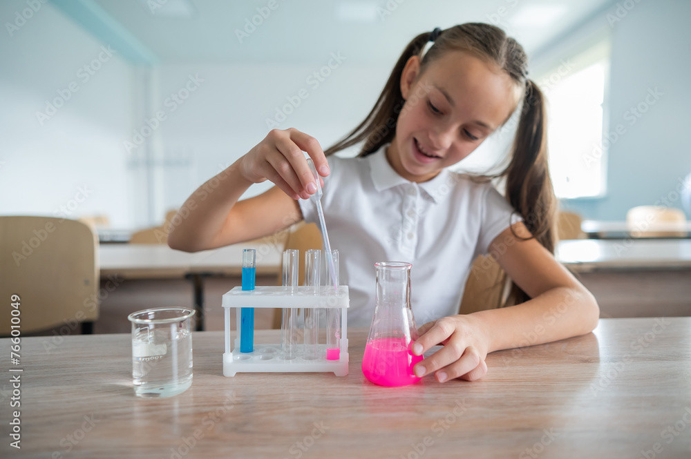 A schoolgirl conducts experiments in a chemistry lesson. Girl pouring colored liquids from a beaker. A schoolgirl conducts experiments in a chemistry lesson. Girl pouring colored liquids from a beaker.