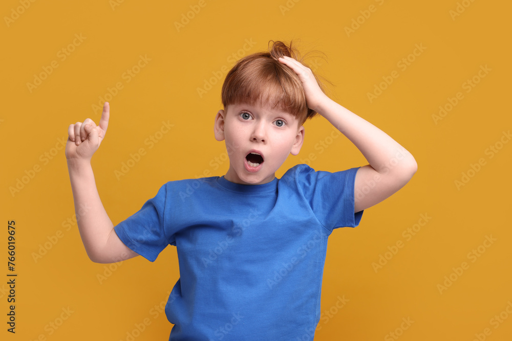 Surprised little boy pointing at something on orange background Surprised little boy pointing at something on orange background