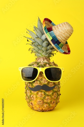 Pineapple with Mexican sombrero hat, sunglasses and fake mustache on yellow background