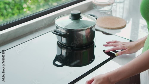 Close-up of hands adjusting temperature on modern induction stove with stainless steel pot, concept of home cooking
