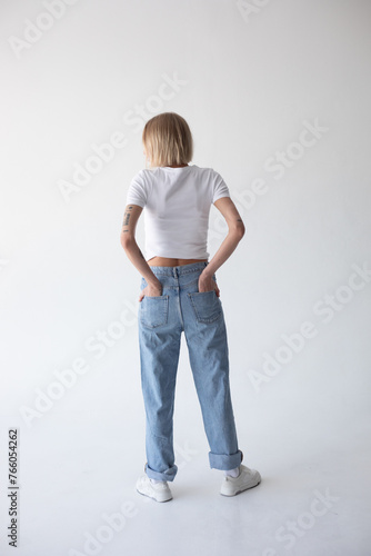 Beautiful blonde girl in a white T-shirt and blue jeans and sneakers posing on a white background