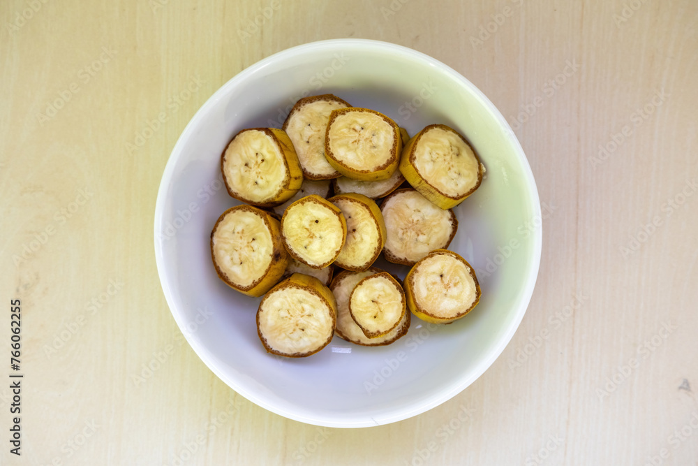 Banana slices in a bowl over wooden background. Healthy natural vitamin snack. Top view.