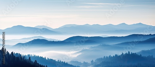 A breathtaking natural landscape featuring a foggy mountain range with trees in the foreground, under a cloudy sky with cumulus clouds