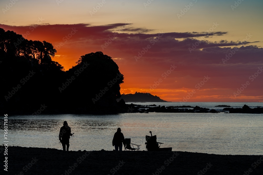 Holidaying People around a campfire at sunset Maraehako Bay, Bay of Plenty, New Zealand.
