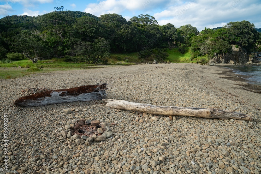 Campfire and driftwood on stoney shoreline. Maraehako Bay, Bay of Plenty, New Zealand.