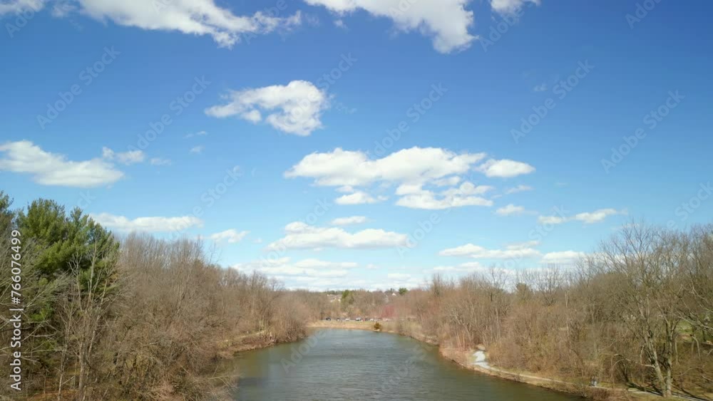 Aerial drone view ascending from river. Trees and bright blue sky with clouds off in the distance. Aerial drone view ascending from river. Trees and bright blue sky with clouds off in the distance.