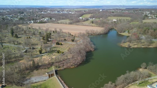 Aerial drone view of a water dam with a cemetery next to it. Mountains and sky visible in the distance. photo