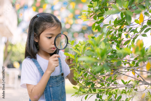 A young girl is looking through a magnifying glass at a leaf