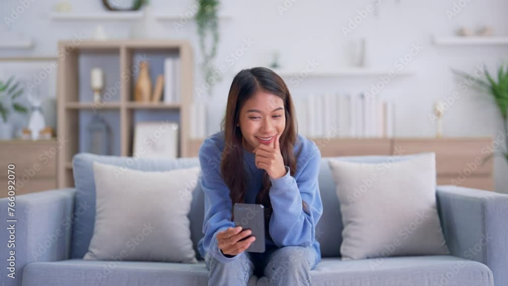 Happy young asian woman relaxing at home. Female smiling and talking chat with friend sitting on sofa and holding mobile smartphone. Girl using video call to close friend Happy young asian woman relaxing at home. Female smiling and talking chat with friend sitting on sofa and holding mobile smartphone. Girl using video call to close friend