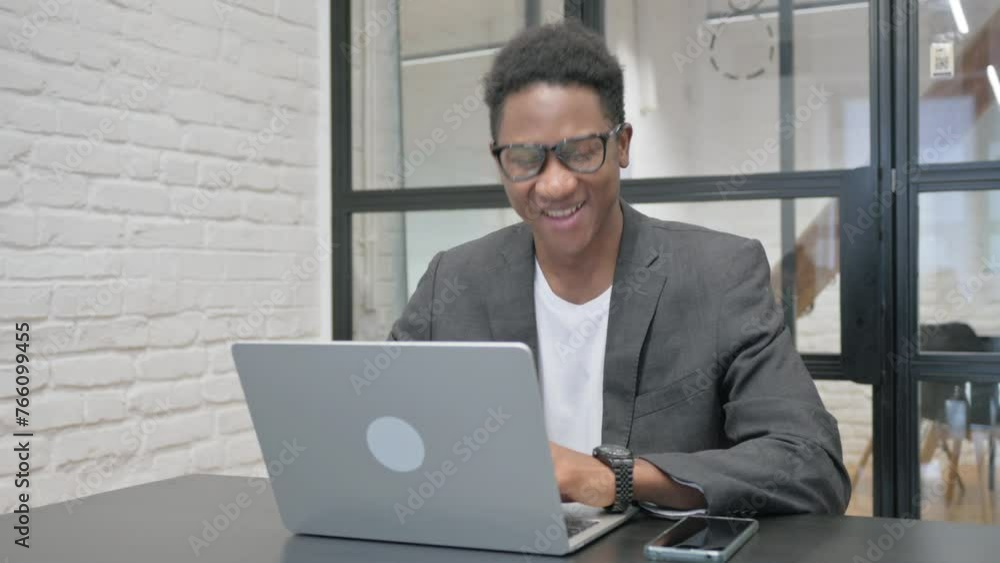 Young African Man Smiling at Camera while Working on Laptop in Office Young African Man Smiling at Camera while Working on Laptop in Office