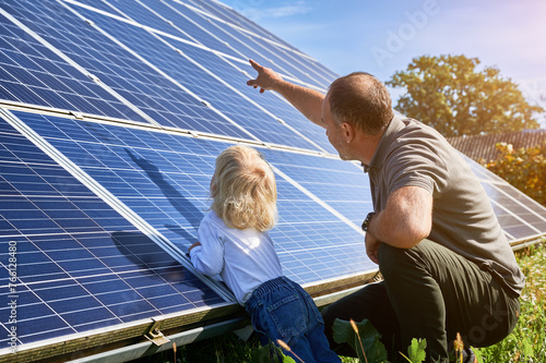 Man showing his son solar panels during sunny day. Father presentng to child modern energy resource. Back view of father and his child watching on solar station.