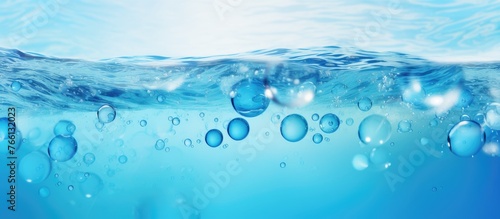 A close up of a liquid wave in the ocean with bubbles rising, against an electric blue sky. The water is freezing cold and transparent