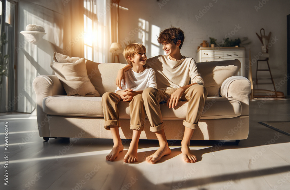 zwei Jungen Heranwachsende sitzen fröhlich lächelnd zueinander gewandt gemütlich barfuß auf einer Couch nebeneinander in hellem Licht der goldenen Stunde Wohnzimmer Freizeit Hobby gemeinsam genießen zwei Jungen Heranwachsende sitzen fröhlich lächelnd zueinander gewandt gemütlich barfuß auf einer Couch nebeneinander in hellem Licht der goldenen Stunde Wohnzimmer Freizeit Hobby gemeinsam genießen