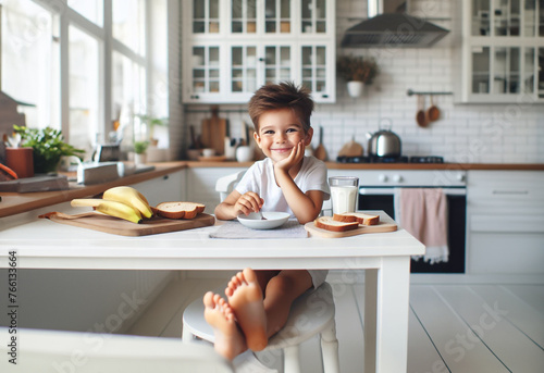 Junge Kind Heranwachsender sitzt fröhlich glücklich lächelnd barfuß am Tisch Frühstück zu Hause in hell Ausstattung Kindheit Ernährung Genuß Freude, Start in den Tag, Küche lebensstil frühstücken photo