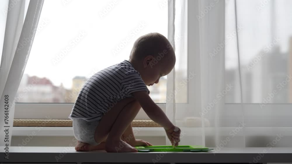 3-year-old child at the window drawing with pen on electronic drawing writing board. Little boy playing with drawing tablet for kids. 3-year-old child at the window drawing with pen on electronic drawing writing board. Little boy playing with drawing tablet for kids.