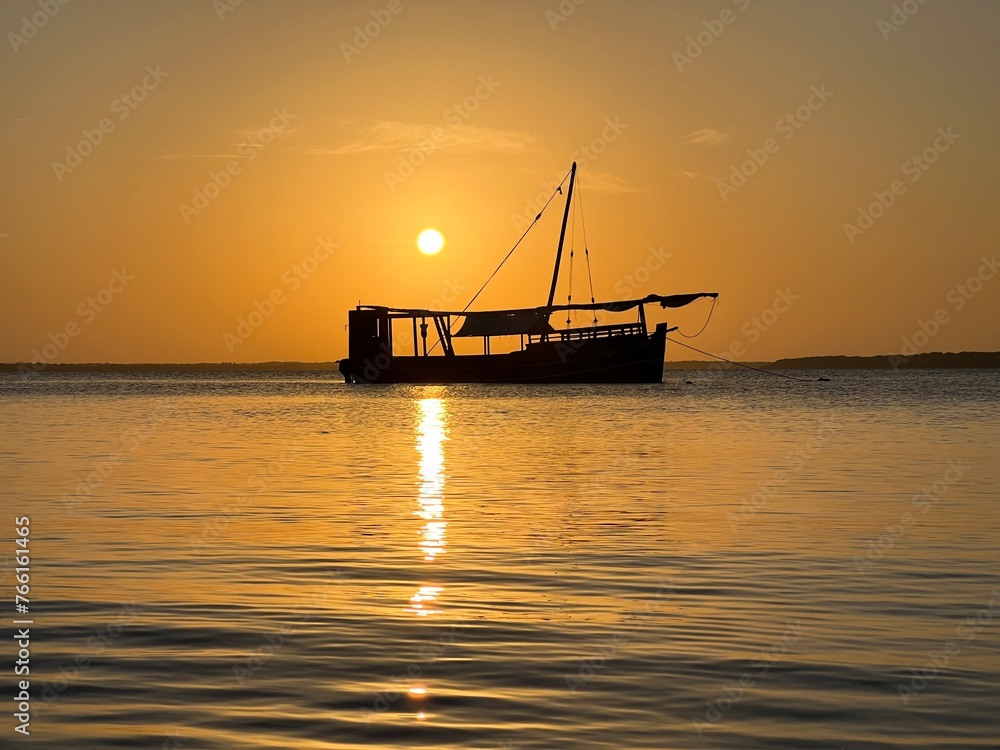 A traditional Swahili Dhow with the sun setting behind it.