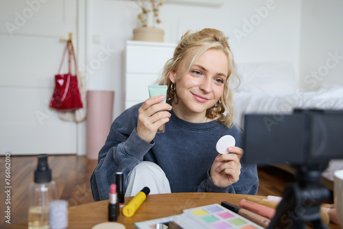 Portrait of young woman promoting beauty product, applies makeup in front of camera, recording video for her vlog, creating content for social media, sitting in a room on floor