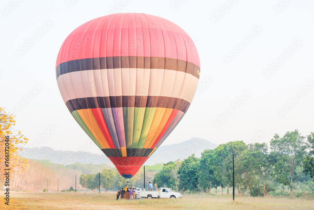 Naklejka premium CHIANG RAI, THAILAND - JANUARY 20, 2024 : Hot air balloon over yellow flower fields against blue sky,Colorful Hot air balloons flying over the valley with blue sky,Travel and Tourism concept.