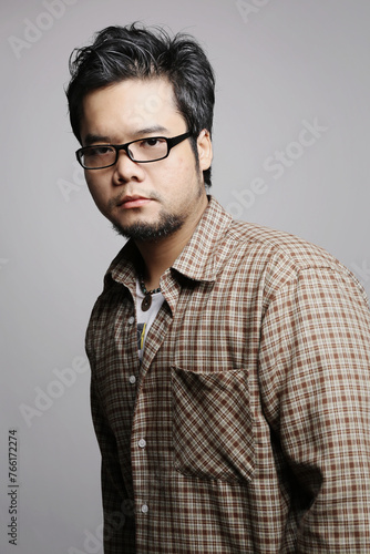 dark tone close up portrait of an Asian man wearing glasses and a beard, with a serious face and gaze