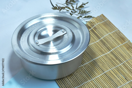 Stainless steel pot placed on a pot holder made from bamboo. Below is a white-blue background