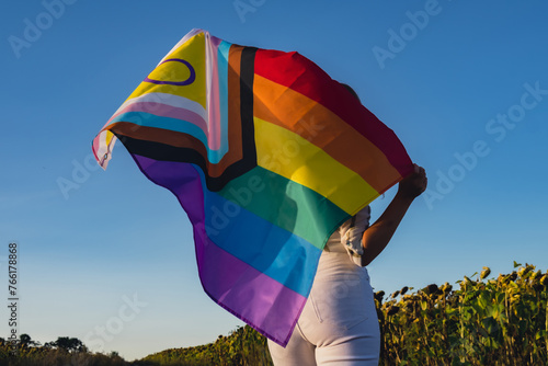 Girl showing her gender identity. Young woman stand with pride flag Rainbow LGBTQIA flag made from silk material on field background. Symbol of LGBTQ pride month. Equal rights. Peace and freedom photo