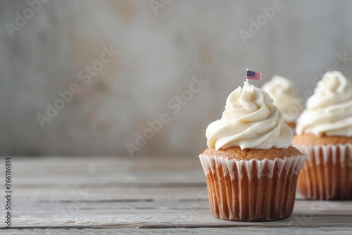 Tasty cupcakes with white cream and USA flag on a grey wooden table against a blurred background