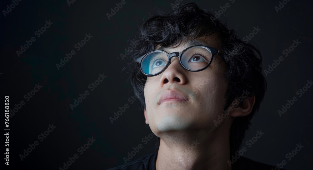 Fototapeta premium A asian man with glasses is standing in front of a black background. He is smiling and looking at the camera. Portrait of a young asian man wearing glasses on dark background