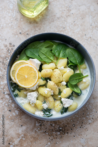 Potato gnocchi with spinach and feta served in a grey bowl, vertical shot on a beige granite background, high angle view
