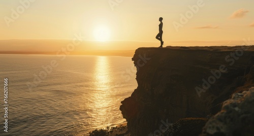 Silhouette of a person standing on one leg, practicing yoga on a cliff overlooking the ocean at sunset, embodying balance and serenity. © radekcho