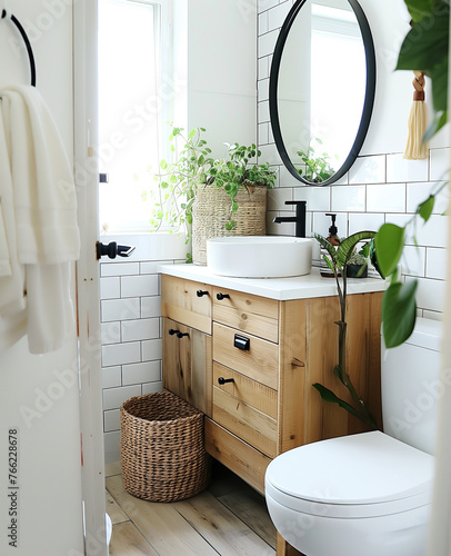 A bright and airy small bathroom with white tiles, a light wood vanity with a black faucet and a round mirror above it, plants on the counter top, a toilet in the corner of the room, a wicker basket.