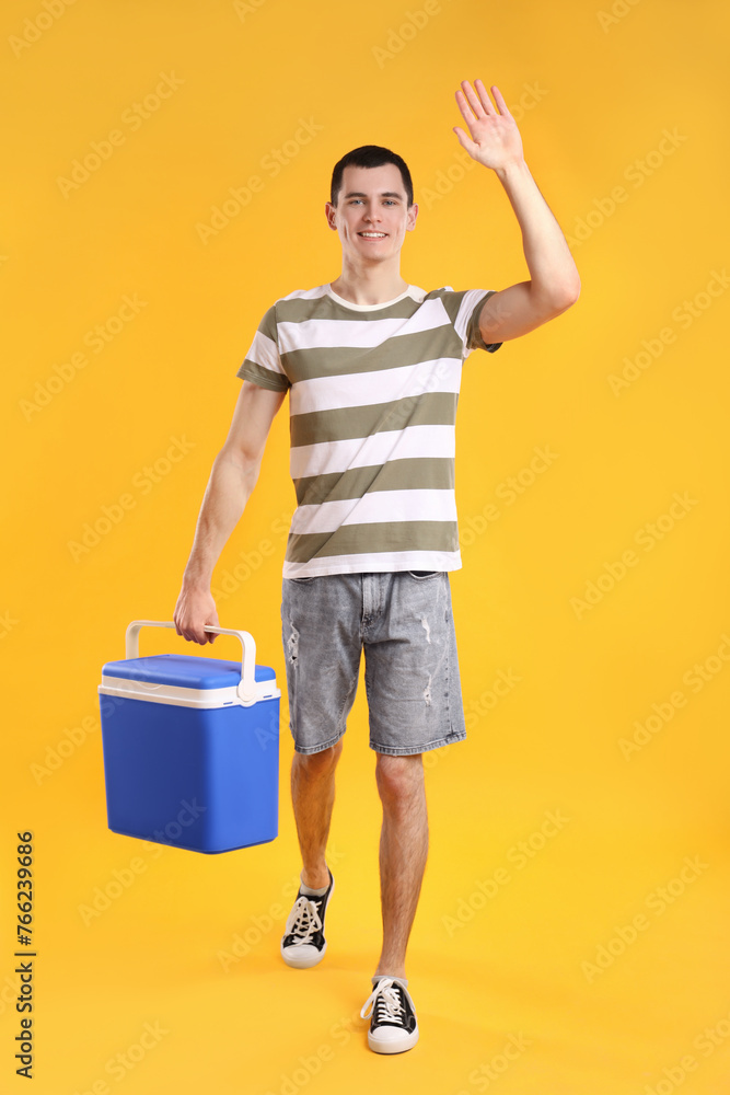 Man with blue cool box walking and greeting someone on orange background Man with blue cool box walking and greeting someone on orange background