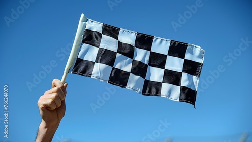Hands raise a checkered flag against a clear blue sky