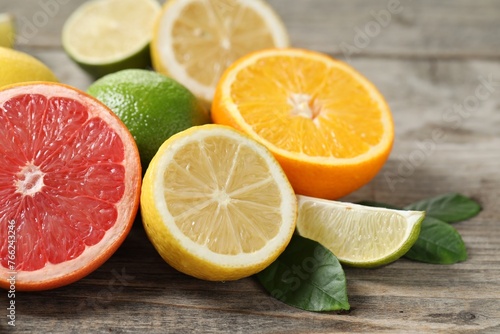 Different fresh citrus fruits and leaves on wooden table, closeup