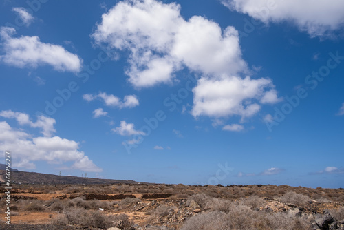 Deserted landscape on the outskirts of the village of Arrieta. Dry bushes, red earth and mountains in the background. Large white clouds. Village of Arrieta. Lanzarote, Canary Islands, Spain