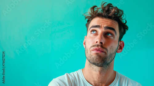 Hombre con el pelo revuelto mira al cielo con cara de sorpresa, sobre un fondo azul photo