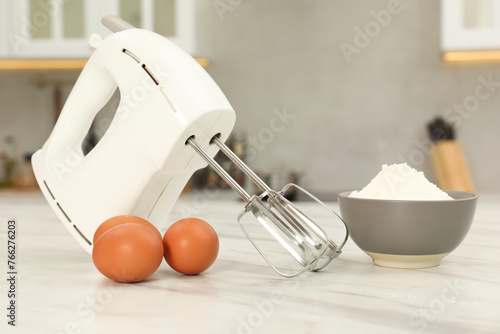 Modern mixer, eggs and bowl with flour on white marble table in kitchen